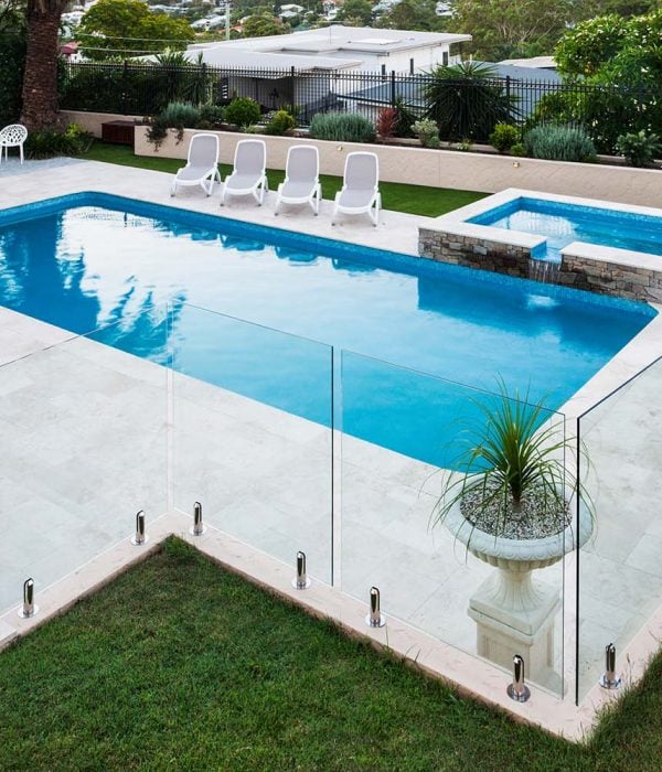 Modern swimming pool covered with glass panels beside a green lawn garden including trees and chairs